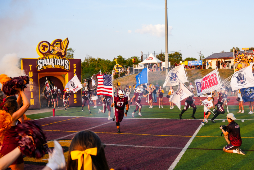turpin football player runs out of the tunnel holding the American flag before a game